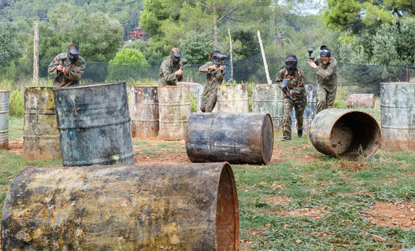 Team of adult people playing paintball on battlefield outdoor, running with guns