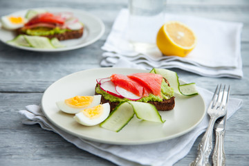 Two smorrebroad sandwiches with red fish,Avocado,eggs and cucumber on plate on a table