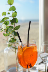 Aperol Spritz and eucalyptus twig in vase standing on the table in cafe on the beach near by sea in the sunny day