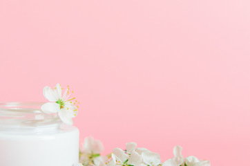 Face cream in white jar on a pink background with white flowers. Concept natural cosmetics, organic...