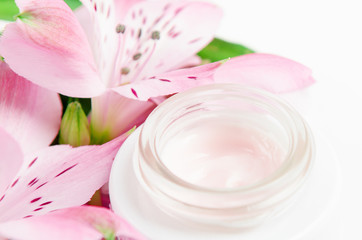 Obraz na płótnie Canvas Face cream in white jar on a white background with pink flowers. Concept natural cosmetics, organic beauty, flower arrangement.