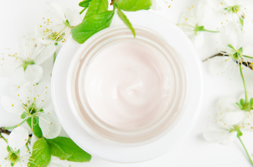Obraz na płótnie Canvas Face cream in white jar on a white background with small flowers of an apple tree. Concept natural cosmetics, organic beauty, flower arrangement. Top view, flat lay.