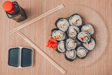 Sushi rolls on a round plate with sticks and soy sauce, top view
