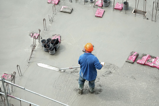 Des ouvriers en ma&ccedil;onnerie s'affairant sur une dalle de b&eacute;ton d'un immeuble en construction