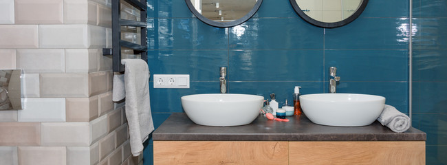 Modern bathroom interior with a wooden shelf, two sinks standing on it and round mirrors....