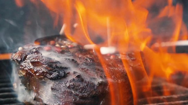 Large grains of pepper fall on juicy grilled filet mignon. Hot juicy oil steak cooking. Caucasian kitchen tasty beefsteak, delicious juicy meat. Street food cooked on hot plate. close up slow motion