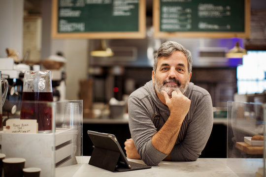 Portrait of owner with tablet computer leaning on counter in cafe
