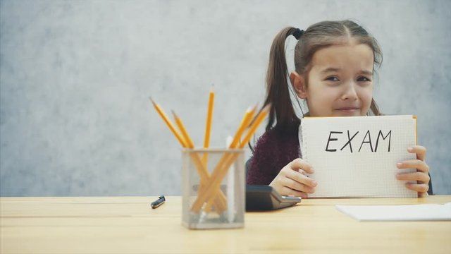 Young, hard-haired girl sitting at the table. During this inscription in the hands of the exam. Has a deplorable look.