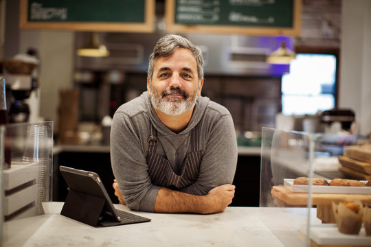 Portrait of smiling male owner with tablet computer on bar counter standing in cafe