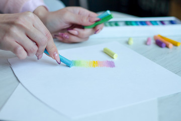 Close-up of female hands are drawing with multicolored chalks on a white sheet, a box with crayons