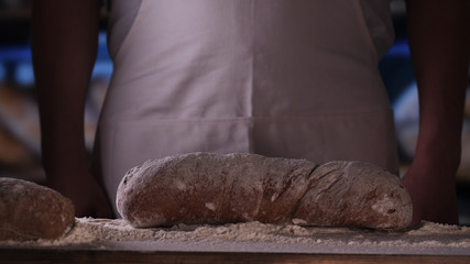 In the bakery, a baker blows off flour from bread, a lot of flour in the air. Concept of: Dirty hands, Flour, Chef, Baker.