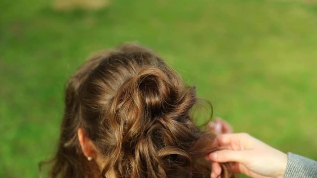 Stylist applying a circle to her hair and preparing a braid for a model with long brown hair outside during a sunny day