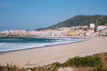 Wide empty beach with beautiful waves and white town on background. Vila Praia de Ancora, Portugal, landmark. Panoramic Atlantic Ocean coast with calm beach. White sand shore. Europe travel concept.
