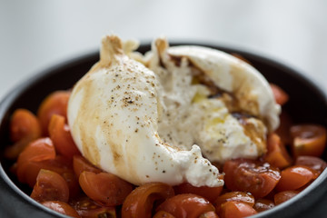 Burrata Büffelmozzarella Kugel mit Tomaten, Olivenöl und Balsamico auf schwarzen Teller
