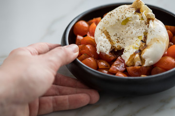 Frau isst Burrata Büffelmozzarella Kugel mit Tomaten, Olivenöl und Balsamico auf schwarzen Teller