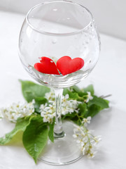 A glass of wine with two hearts on a light background. selective focus. Holiday concept. A branch of bird cherry.