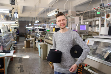 close up photo of a young man with black threads in cones in his hands near industrial knitting machines