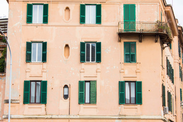 Fototapeta na wymiar Facade of residential building with big green windows with shutters. Architecture and beauty of roman capital city, of Rome, Italy.