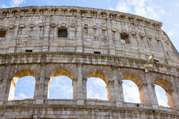 Fototapeta premium Coliseum wall and arches fragment on the front, on the foreground, bright light of sun through the wall of Colosseum. Bright blue sky on the background. Rome, Italy.