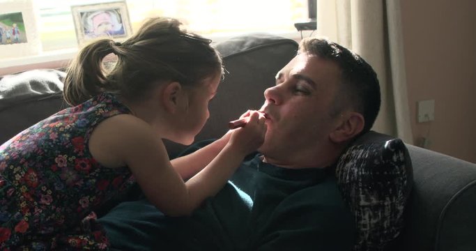 Young daughter putting lipstick on her dad