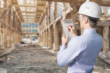 Engineer taking a note. Focused man in white hardhat holding a clipboard and writing.