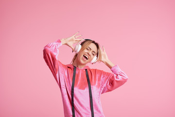 Obraz na płótnie Canvas Wireless connection. Portrait of young woman posing isolated over pink background listening fun music with headphones.
