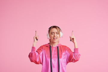 Wireless connection. Portrait of young woman posing isolated over pink background listening fun music with headphones. Shows fingers up. Space for text