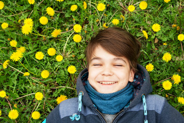 Cheerful teenager lies in dandelions with closed eyes. Spring, summer, green grass