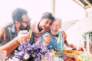 Happy people family concept laugh and have fun together with three different generations ages : grandfather father and young teenager son all together eating at lunch - Powered by Adobe