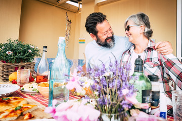 Happy family caucasian people couple mother son senior adult age concept with hug and fun between man and woman smiling - lunch time at home or restaurant with table
