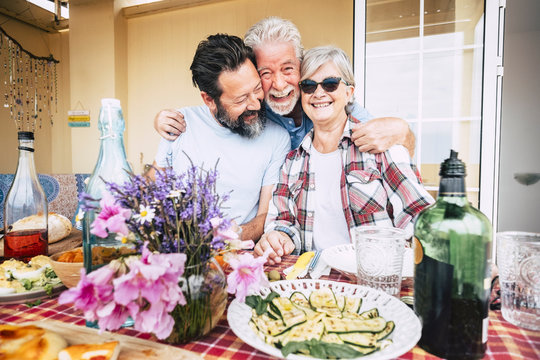 Happy family people aged senior adult portrait hugging and having fun in front of a table full of food and beverages ready to celebrate all together in friendship and happiness