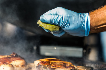 The chef squeezing lemon juice onto grilling steak. Fresh, delicious grilled meat