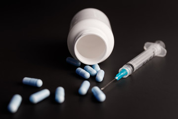 Close up view of a syringe with hypodermic needle and generic blue pills. Opiate and heroin overdoses have skyrocketed in recent years II