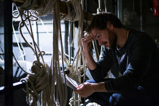 Actor crouching on fly loft at theatre studying script
