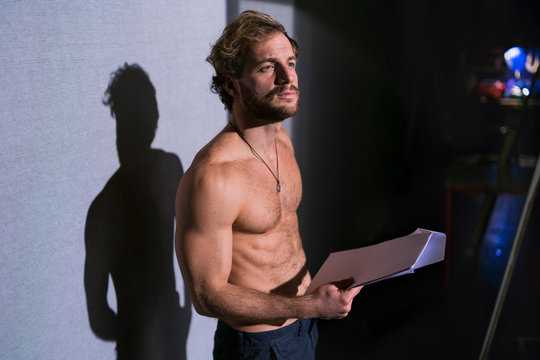 Portrait of shirtless actor with script rehearsing at theatre