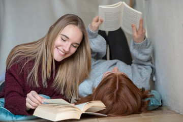 Two friends lying side by side on the floor reading books