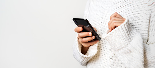 A young woman in a white sweater holds a smartphone in her hands, chooses something looking at the...