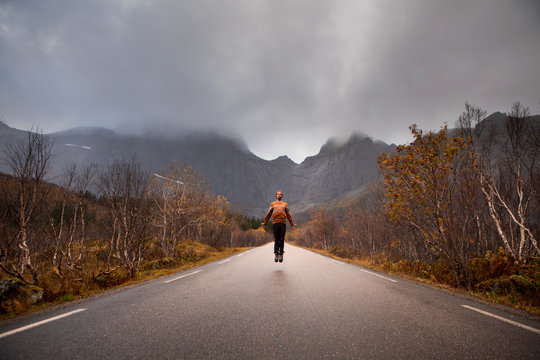 Norway, Lofoten Islands, man jumping on empty road surrounded by rock face