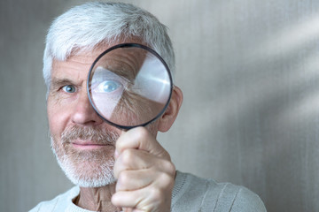 Fototapeta na wymiar a gray-haired man in light clothes looking through a magnifying glass
