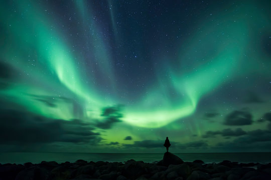 Norway, Lofoten Islands, Eggum, man standing on rock and watching northern lights