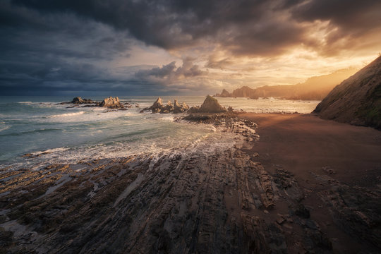 Scenic view of empty beach with stones and waves on sundown background with rain clouds