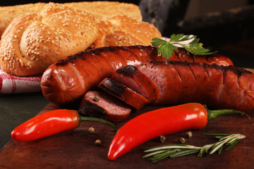 Grilled sausages with vegetables, spices and bread on wooden cutting board background