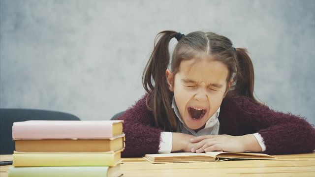A schoolgirl girl sits on a gray background. During this time the schoolboy reads the book carefully. Diligent student Reading asleep.