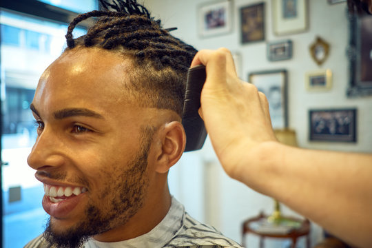 Crop view of Anonymous hairstylist doing a modern haircut to a cheerful african-american customer
