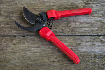 Gardeners hand tool - red pruner. Garden tools lying on a wooden table. Open pruner.
