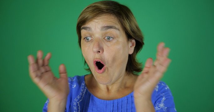 An adult woman is surprised by something and puts her hands to her chin while