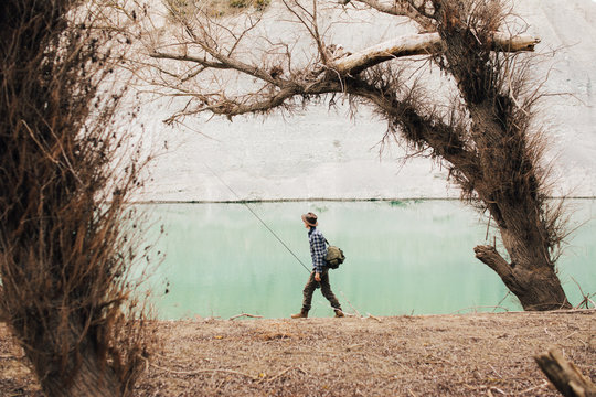 Side view of male with backpack standing on lake shore and fishing on sunny day in nature