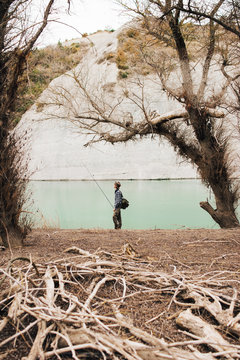 Side view of male with backpack standing on lake shore and fishing on sunny day in nature