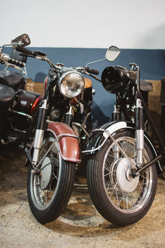 Shabby vintage motorbikes with broken headlights parked inside repair workshop
