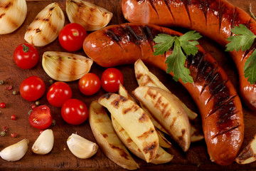 Grilled sausages with vegetables, spices and bread on wooden cutting board background